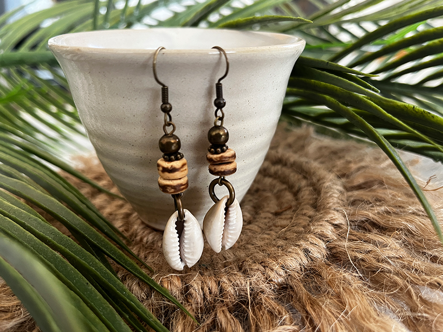 Boho chic cowrie shell earrings artfully arranged on a pottery cup