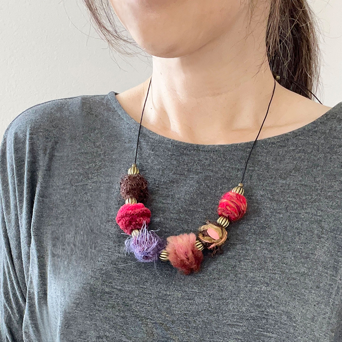 Woman wearing a shade of red yarn-wrapped statement necklace