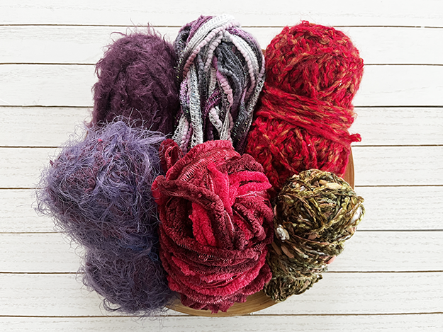 A picture of six different shades of reddish and purplish yarns